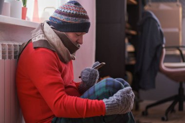 Evde üşüyen bir adam evde ısıtma sorunu yaşıyor. Telefonla oturuyor..