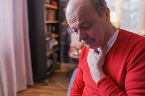 Senior man having sore throat and touching his neck at home — стоковое фото
