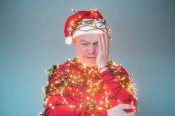 Frustré homme âgé en chapeau de Noël et guirlande touchant sa tête — Photo