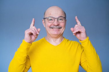 Heyecanlı adam mavi stüdyo arka planını işaret ediyor.