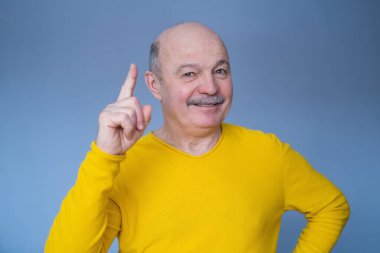 Heyecanlı adam mavi stüdyo arka planını işaret ediyor.