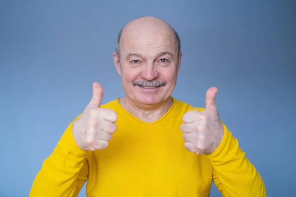 Handsome senior man in yellow sweater shows thumb up. Royalty Free Stock Images