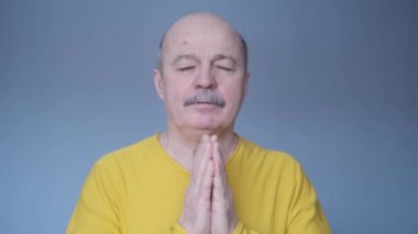 Tecrit edilmiş mavi arka plandaki kıdemli adam avuç içlerini bir arada tutar..