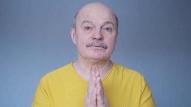 Tecrit edilmiş mavi arka plandaki kıdemli adam avuç içlerini bir arada tutar..