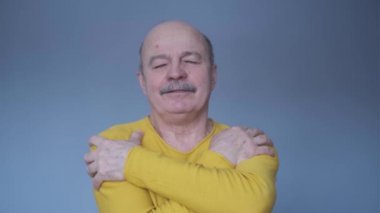 Kendine güvenen, gülümseyen, kendini kucaklayan adam mavi duvarın arkasında tek başına.