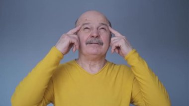 Mavi duvarda tek başına duran, parmaklarını şakaklara koyan düşünceli kıdemli adam.