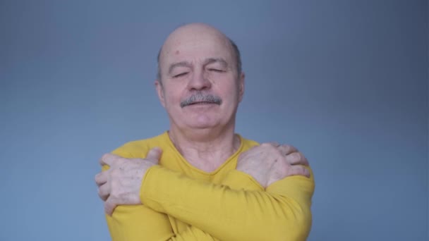 Уверенный улыбающийся мужчина, обнимающий себя на фоне синей стены — стоковое видео