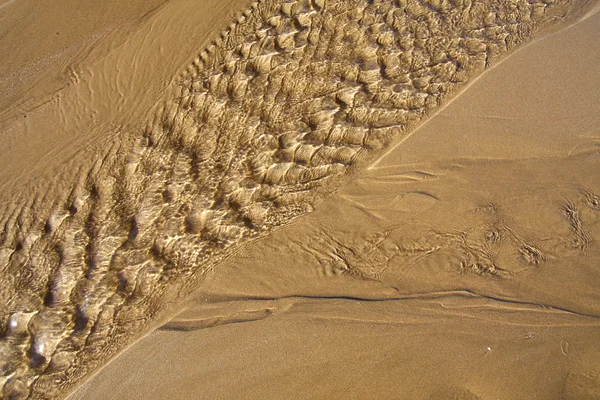 Water rimpelingen over een zandstrand — Stockfoto
