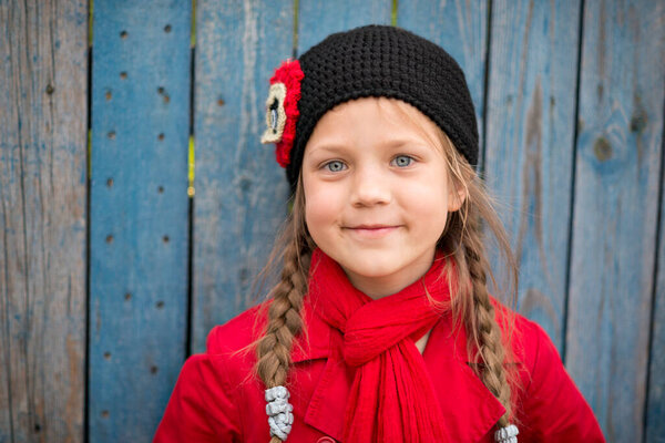 portrait of smiling girl in red raincoat and scarf near wooden fence