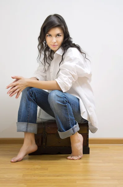 Beautiful brunette sitting on the coffer. — Stock Photo, Image