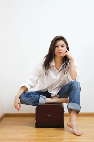 Beautiful brunette sitting on the coffer. — Stock Photo, Image