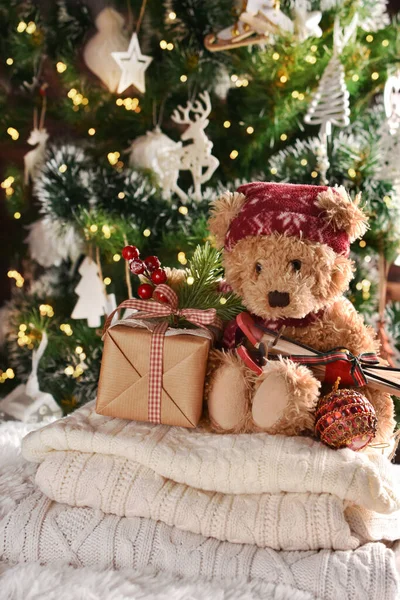 圣诞节依旧 可爱的泰迪熊坐在冬天的毛衣上 圣诞树前还有一个礼品盒 — 图库照片