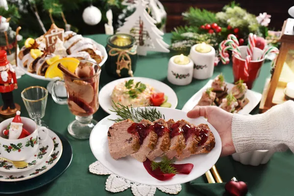 一只手拿着一个装有传统圣诞覆盆子的盘子 放在摆满圣诞前夜菜的节日桌上 — 图库照片
