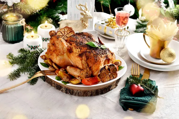 用土豆 西红柿和大蒜在圣诞桌上烤整只鸡 配有节日装饰和白色亚麻布桌布 — 图库照片