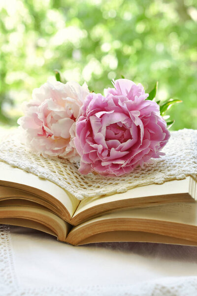 Romantic style still life with two pink peonies lying on old books on the table in the garden