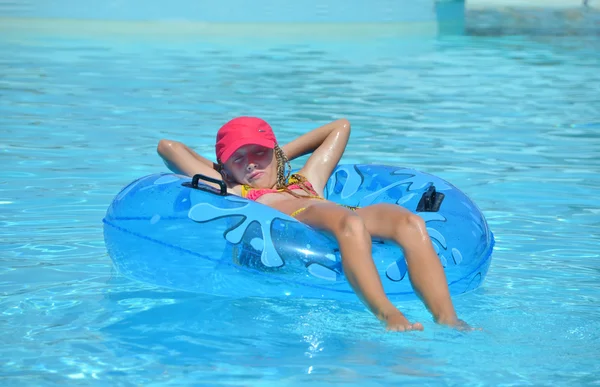 Girl in a pink cap lying on an inflatable disc in the pool. — Stock Photo, Image