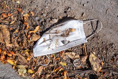 used and dirty disposable face mask on the ground