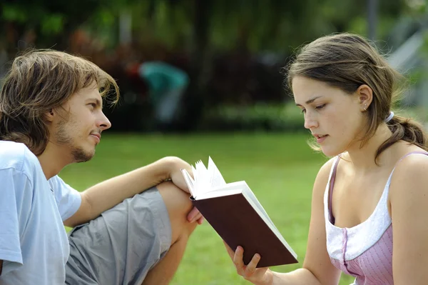 En pojkvän och flickvän läser en bok i en park — Stockfoto