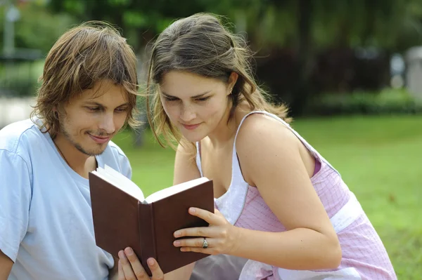 En pojkvän och flickvän läser en bok i en park — Stockfoto