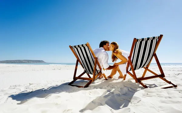 Summer beach kissing couple sitting on deck chairs enjoying an intimate moment — Stock Photo, Image