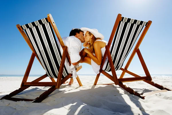 Summer beach kissing couple sitting on deck chairs enjoying an intimate moment — Stock Photo, Image