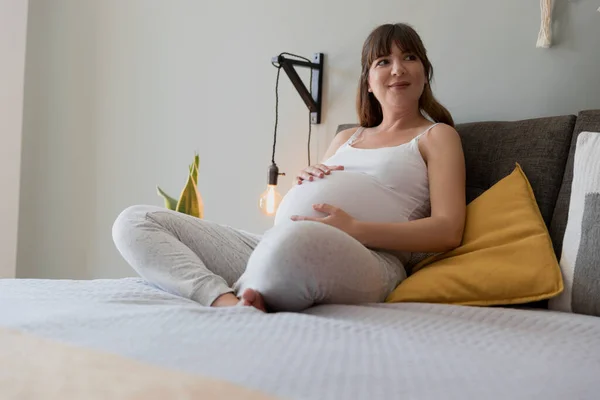 快乐的孕妇坐在床上 在家里摸着肚子 — 图库照片