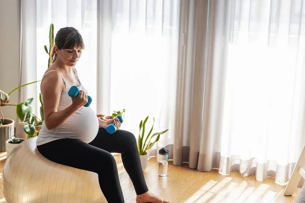 Hamile Kadın Dambıllarla Çalışıyor Evde Bir Fitbol Topunda Güç Egzersizleri — Stok fotoğraf