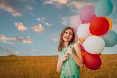 Young woman in the field holding colorful balloons
