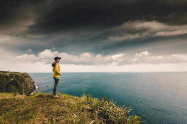 Woman watching the ocean with a lighthouse on the back, Azores Island. clipart