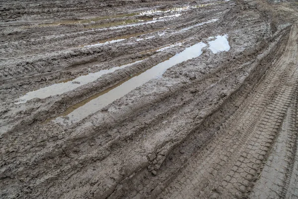Uma estrada rural quebrada depois da chuva. Pudim depois da chuva em uma estrada de terra. Argila, solo e poças na luz do dia nublado após a chuva, estação de outono. — Fotografia de Stock