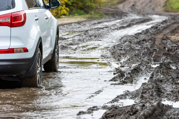 Czysty biały samochód SUV poruszający się po brudnej drodze z mokrą gliną przed rozmazanym stoku — Zdjęcie stockowe