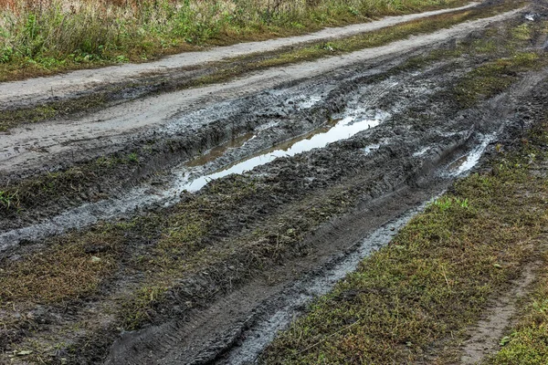 Uma estrada rural quebrada depois da chuva. Pudim numa estrada de terra. Argila, solo e poças na luz do dia nublado após a chuva, estação de outono. — Fotografia de Stock