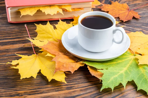 Coffe cup on wooden table with book and colorful autumnal maple leaves — Stock Photo, Image