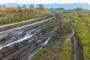 Sonbahar sisli sabahları ön planda toprak yol ve arka planda tepe üzerinde küçük binalar olan rustik lansdcape