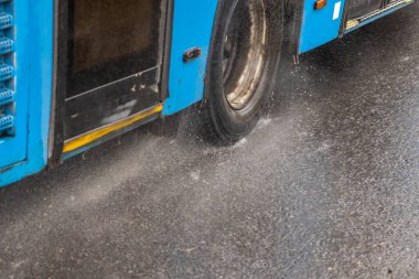 Mavi belediye otobüsü yağmur damlalarıyla yağmurlu yolda ilerliyor