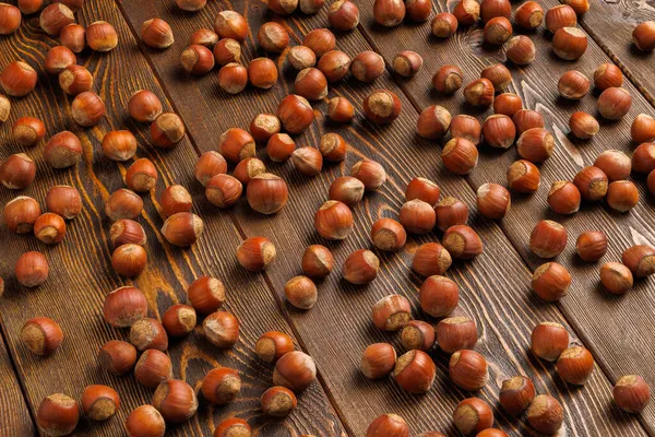 Lískové ořechy s skořápkami rovnoměrně roztroušené na hnědém dřevěném povrchu stolu — Stock fotografie