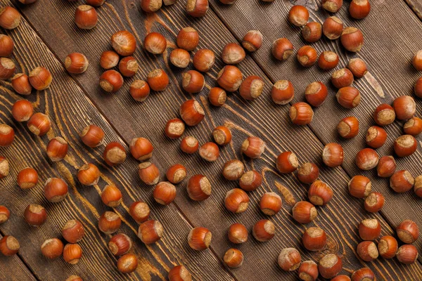 Muitas avelãs com conchas uniformemente espalhadas na superfície de madeira marrom — Fotografia de Stock