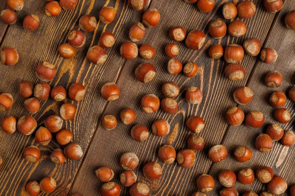 Many hazelnuts with shells evenly spread out on brown wooden surface — Stock Photo, Image