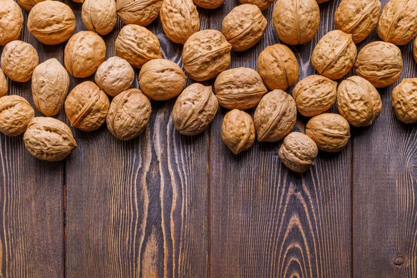 Muchas nueces con conchas dispersas al azar en la superficie de madera marrón con espacio de copia en la parte inferior de la imagen — Foto de Stock