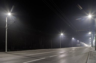 Boş sisli gece yolu ve sıra sıra lamba direkleri