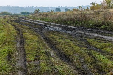 Sonbahar sisli sabahları ön planda toprak yol ve arka planda tepe üzerinde küçük binalar olan rustik lansdcape