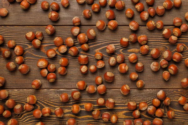 Багато лісових горіхів з мушлями рівномірно розкидані на коричневій дерев'яній поверхні — стокове фото