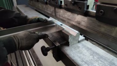 Bükme makinesinde kalın bir metal levhayı bükmek, yakın çekim. Makine operatörü bir levhayı büküyor.
