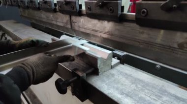 Bükme makinesinde kalın bir metal levhayı bükmek, yakın çekim. Makine operatörü bir levhayı büküyor.