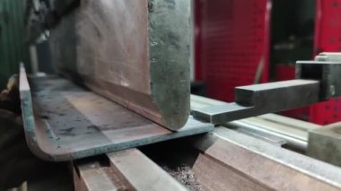 Bükme makinesinde kalın bir metal levhayı bükmek, yakın çekim. Makine operatörü bir levhayı büküyor