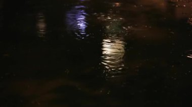 Gece yağmur birikintisi, içine su damlaları düşen siyah bir asfalt üzerinde.