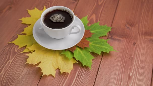 Koffiekopje op houten tafel met kleurrijke herfstesdoornbladeren met draaiende koffiebelletjes — Stockvideo