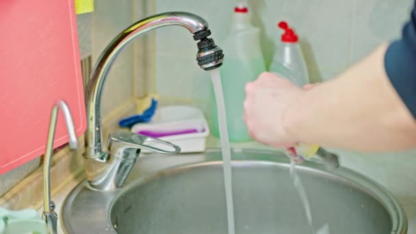 Hombre caucásico desnudo lavando dos cucharas y un tenedor con detergente de jabón líquido y esponja azul-amarilla — Vídeos de Stock