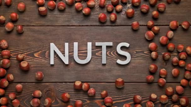 Das Wort Nüsse auf Holzbrett umgeben von rumpelnden Haselnüssen — Stockvideo
