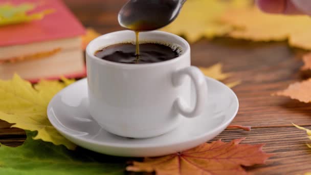 Hand roeren koffie met lepel in kopje op houten tafel met boek en kleurrijke herfstesdoorn bladeren — Stockvideo